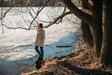 The girl stands at the frozen lake in the spring.