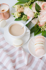Elegant sweet dessert macarons, cup of coffee and pastel colored beige flowers bouquet