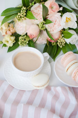 Elegant sweet dessert macarons, cup of coffee and pastel colored beige flowers bouquet