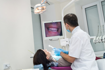 Dentist examining patient's teeth with camera, looking at screen
