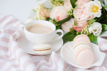 Elegant sweet dessert macarons, cup of coffee and pastel colored beige flowers bouquet