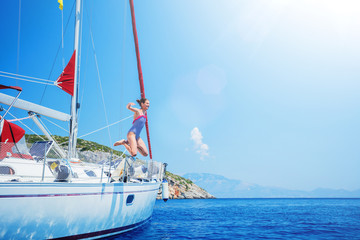 Girl jump in sea of sailing yacht on summer cruise. Travel adventure, yachting with child on...