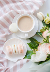 Elegant sweet dessert macarons, cup of coffee and pastel colored beige flowers bouquet