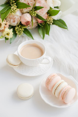 Elegant sweet dessert macarons, cup of coffee and pastel colored beige flowers bouquet