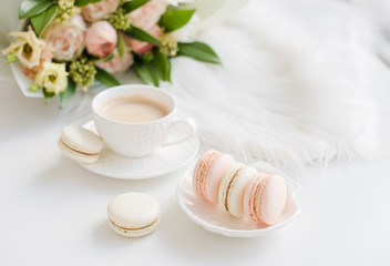 Elegant sweet dessert macarons, cup of coffee and pastel colored beige flowers bouquet