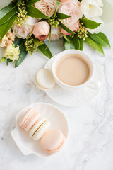 Obraz na płótnie Canvas Elegant sweet dessert macarons, cup of coffee and pastel colored beige flowers bouquet on white marble