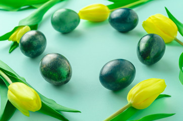 Spring concept with Easter eggs and yellow tulips on turquoise blue background.