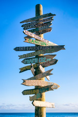 Rustic wooden sign pointing the way to landmark cities against bright blue tropical sky in Key...