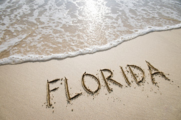 Simple Florida American holiday getaway message written in smooth sand with an incoming wave on a tropical beach