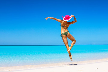 Beautiful girl in a pink hat in a gracegul jump on the beach in Bahamas. Outdoor shot.