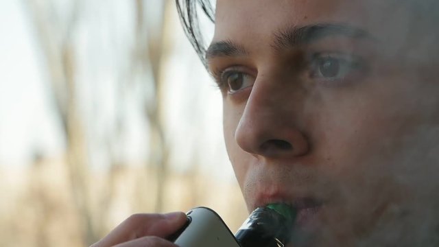 handsome boy smoking e-cigarette outdoors. Face of vaping person in slow motion