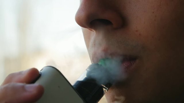 young handsome man vaping outdoors. Macro of smoking person in slow motion