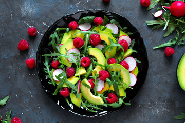 Avocado salad with raspberries, pomegranate, arugula and sesame on dark background. Top view with copy space. Healthy food. Vegetarian and vegan food.