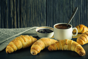 fresh croissants with coffee and jam on a dark wooden background