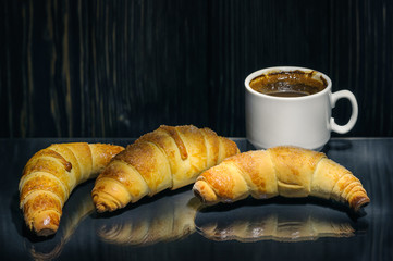 fresh croissants with a cup of coffee on a glass surface on a dark wooden background