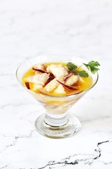white fish ceviche in orange juice, served in a glass ice-cream bowl against a background of white marble. raw fish is marinated in lemon juice and served with onions, citrus juice and greens. 