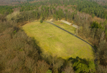Aerial view on hidden football stadium in deep forest, including ruined fan stand, treadmill and gates.