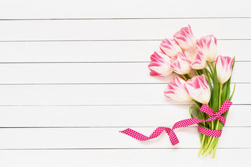 Bouquet of pink tulips decorated with ribbon on white wooden background. Top view, copy space. Greeting card.