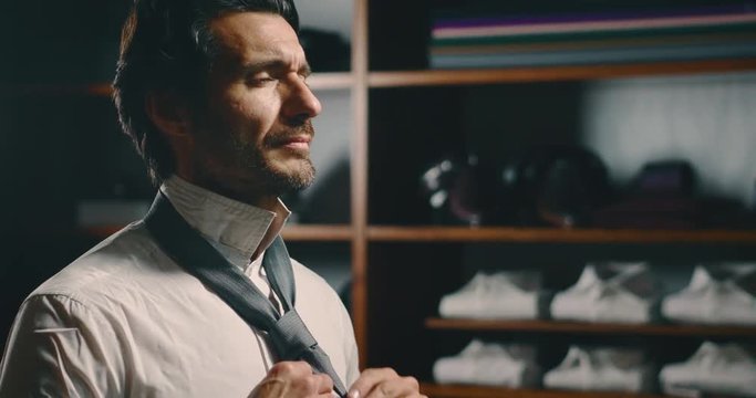 Slow motion of handsome businessman trying a new high quality tailor made suit and first ties a tie in atelier.
