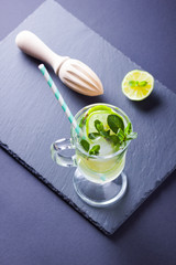 Mojito cocktail on black background. Mojito with lime and fresh mint on slate board. Summer refreshing cocktail and wooden juicer on dark background. Infused water