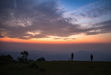 Photographer man standing on hill with sunrise landscape mountain fog mist colorful sky beautiful clouds in the morning silhouettes
