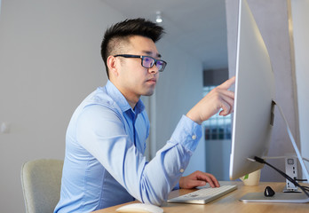 Naklejka premium Young asian blockchain professional wearing shirt and glasses working while sitting in front of desktop computer at coworking office