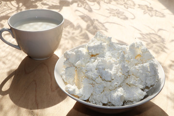A mug of milk and a cup of cottage cheese on a sunny table, a bouquet of flowers for the mood, diet food and a healthy lifestyle in the village