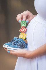 Pregnant woman holding wooden letters and shoes that say boy