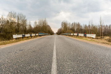 view of the asphalt road across the bridge with side chippers, rural road passes through the forest