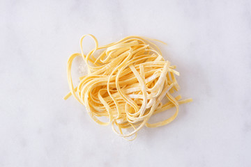Nest of fresh linguine pasta, top view against a white marble background - obrazy, fototapety, plakaty