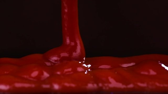 Ketchup pouring over black background. Food backdrop. Tomato red ketchup close-up. Slow motion 4K UHD video