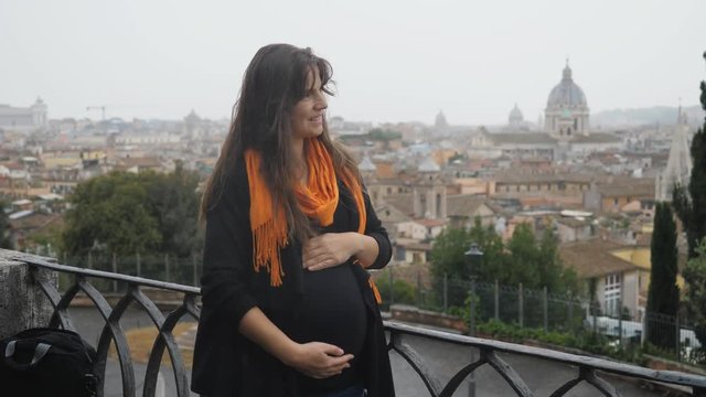 Pregnant happy woman admire up view Rome panorama and caress her belly, travel anytime