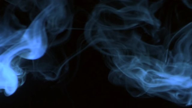 Vertical video screensaver - Trickle blue smoke slowly rising graceful twists up on black background. Cigar smoke blowing from the left side. Closeup, isolated on black background.