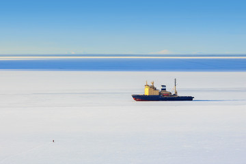 Icebreaker among the ice and a small figure of a man on the ice. Maritime navigation in the north. Cold winter weather. Sea open spaces. Nagaev Bay, Sea of Okhotsk, Magadan, Far East of Russia.