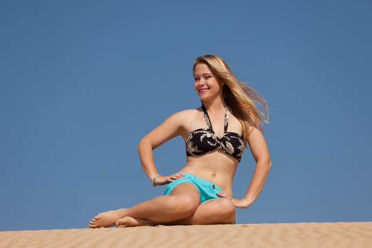 A very happy blonde woman on the beach in her bikini is smiling