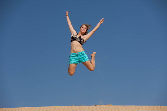A very happy blonde woman on the beach in her bikini is smiling