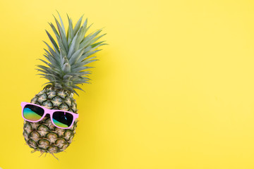 Beach accessories pineapple with pink sunglasses on yellow background for summer holiday and vacation concept.