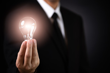 Business concept. Businessman holding lamp Light bulb against dark backgroun.