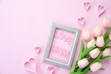 Happy mothers day concept. pink tulip flower with paper heart and Picture Frame with LOVE MOM text on pink pastel background.