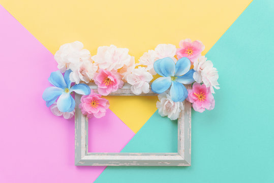 Summer composition. Empty frame and flowers flat lay on yellow, green and pink pastel background with copy space.