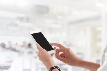 Woman hand holding and using smartphone with blank screen for your text or advertising isolated on blurred co working office interior background.Mock up phone mobile business and technology concept.