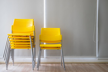 Yellow stacking plastic chairs for meeting or workshop in front of gray background.