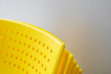 Yellow stacking plastic chairs for meeting or workshop in front of gray background.
