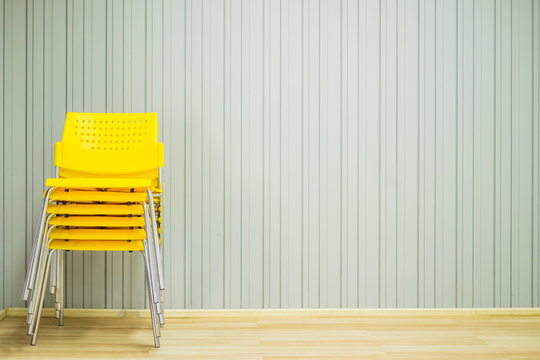 Yellow stacking plastic chairs for meeting or workshop in front of gray background.
