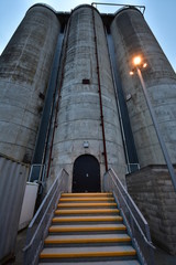 Industrial silo consisting of three tall concrete cylindrical towers interconnected by metal piping...