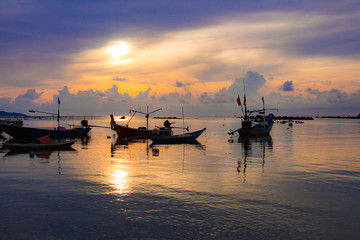Fototapeta premium Fishing boat in the sea, sunset and silhouettes of wooden boats