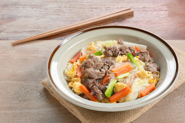 stir fried glass noodle with pork and vegetable in a ceramic dish on wooden table. asian homemade style food concept.