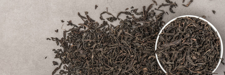 Dried tea is poured into a white ceramic cup on a gray textured background. View from above. Layout.