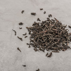 Dried tea is poured scattered on a grey textured background.
