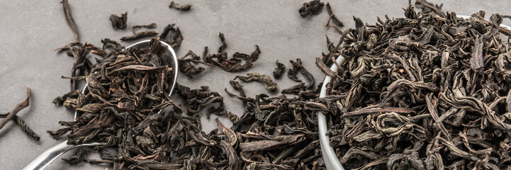 Dried tea in a white ceramic cup with a spoon on a gray textured background.